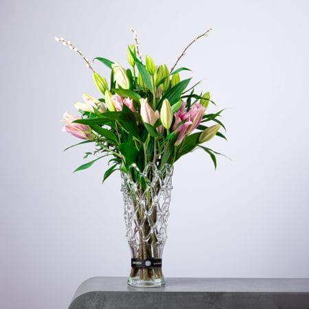 Luxurious lily arrangement with pink oriental lilies and greens in a sculpted crystal vase.