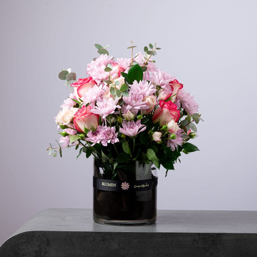 Elegant bouquet of pink chrysanthemums and two-tone roses arranged in a round glass vase.