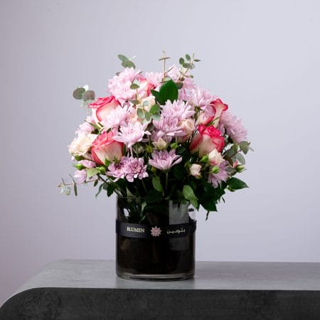 Elegant bouquet of pink chrysanthemums and two-tone roses arranged in a round glass vase.