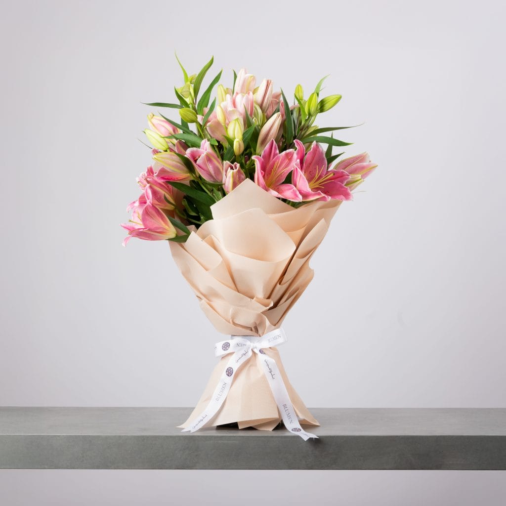 Pink lily bouquet wrapped in beige paper with white ribbon.