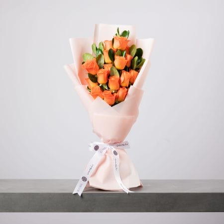 Orange rose bouquet wrapped in blush paper with white ribbon.