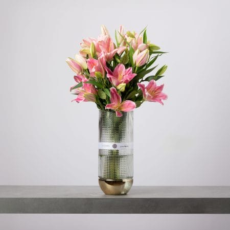 Pink lily arrangement in textured glass vase with gold base.