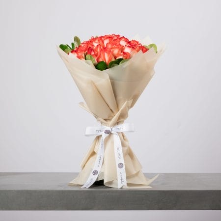 Coral-hued roses bouquet wrapped in soft beige paper