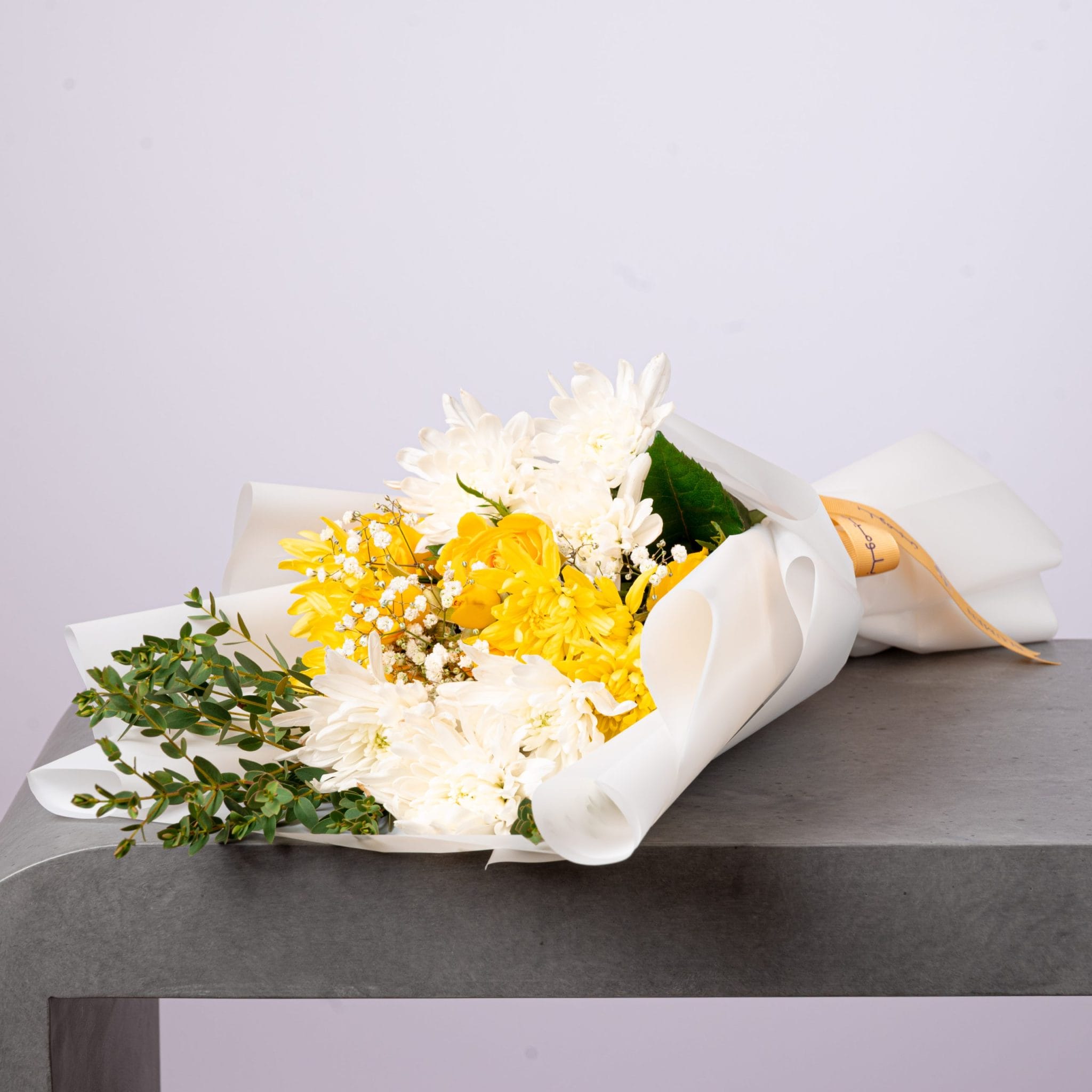 Wrapped bouquet of white and yellow chrysanthemums with greenery.