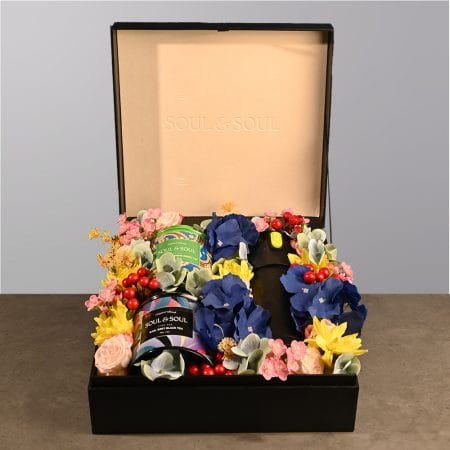 Gift box featuring two tea tins and a thermos surrounded by colorful floral arrangement.