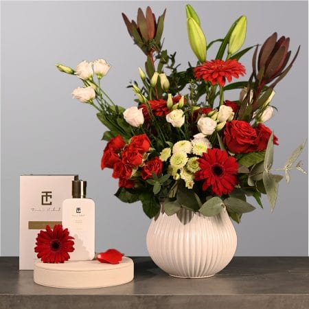 Floral arrangement with red roses, red gerberas, ivory flowers, and greenery in a rounded textured vase.