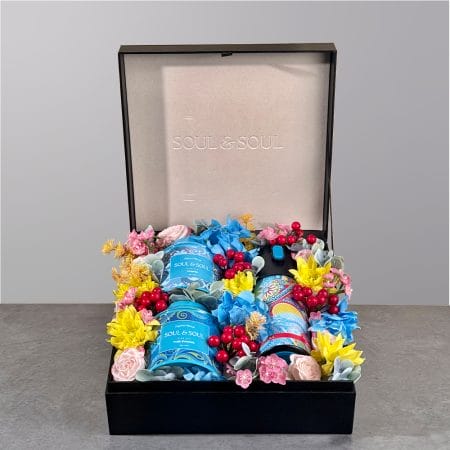 Gift box featuring two tea tins and a thermos surrounded by colorful floral arrangement.