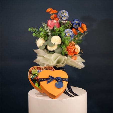 Colorful floral arrangement featuring orange, blue, and ivory flowers with lush greenery in an elegant bouquet.