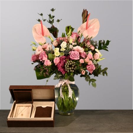A lush floral arrangement in a clear glass vase featuring pink roses, anthuriums, and mixed greenery with a soft blush color palette.