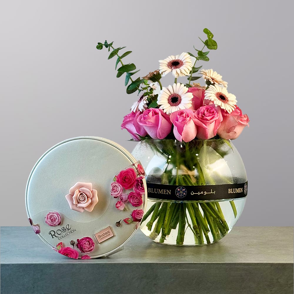 A rounded glass vase filled with soft pink roses and white and peach gerbera daisies, accented with fresh eucalyptus greenery.