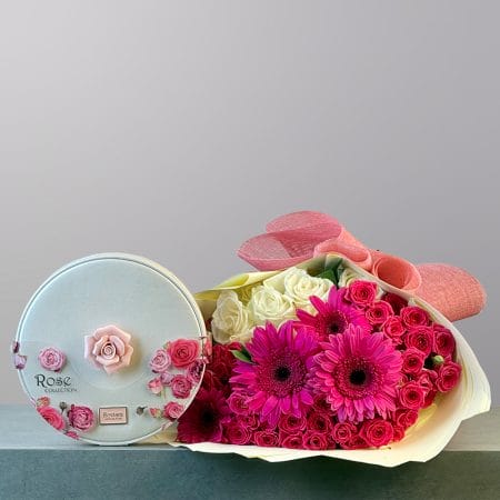 A vibrant bouquet of fuchsia gerbera daisies, hot pink spray roses, and creamy white roses wrapped in elegant coral-pink paper.